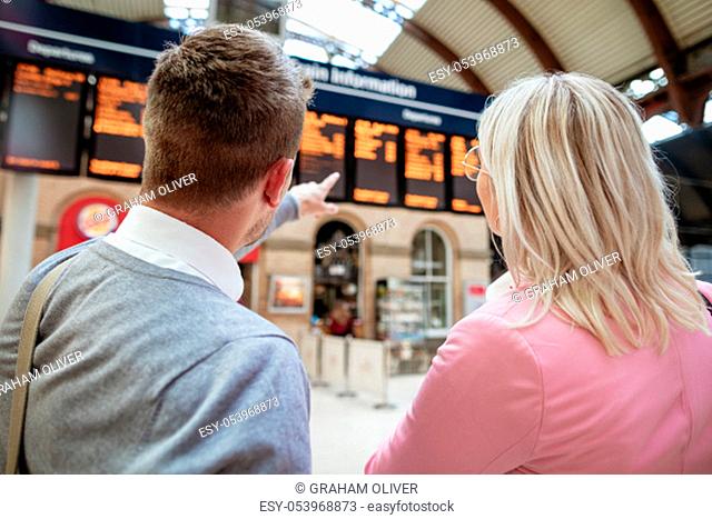 A businessman and businesswoman looking at a departure board in a train station