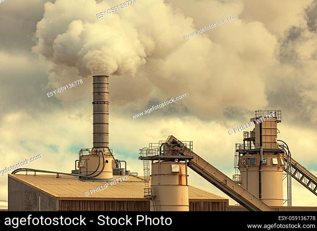 A large manufacturing facility in a regional township with steam coming from the chimney stacks during processing