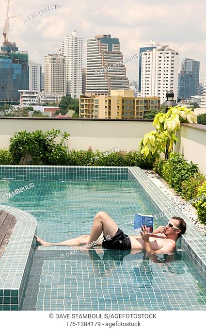 Life at the top, relaxing with a book in a rooftop pool in Bangkok, Thailand