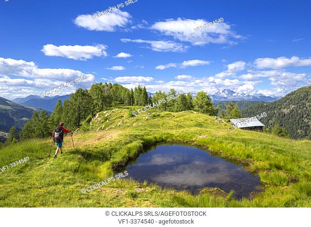 Hiker walks near a hut with alpine pond. Valgerola, Orobie Alps, Valtellina, Lombardy, Italy, Europe