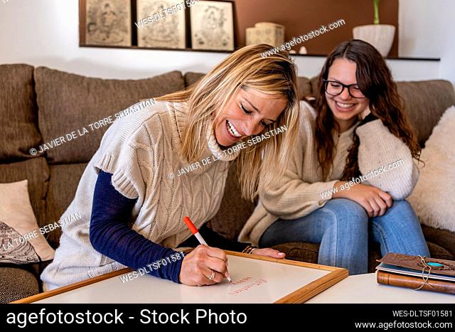 Smiling female psychologist writing on whiteboard while sitting with young woman in office