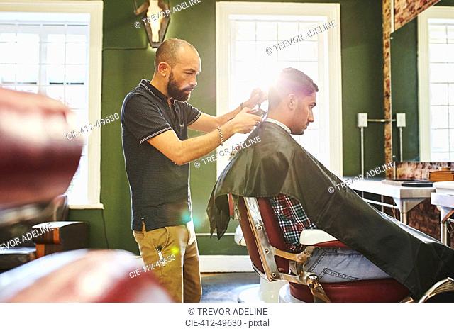 Focused male barber giving customer a haircut in barbershop