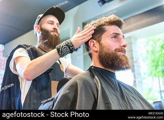 Low-angle view of a handsome bearded young man, ready for a trendy haircut done by an experienced hairstylist in a cool beauty salon for men