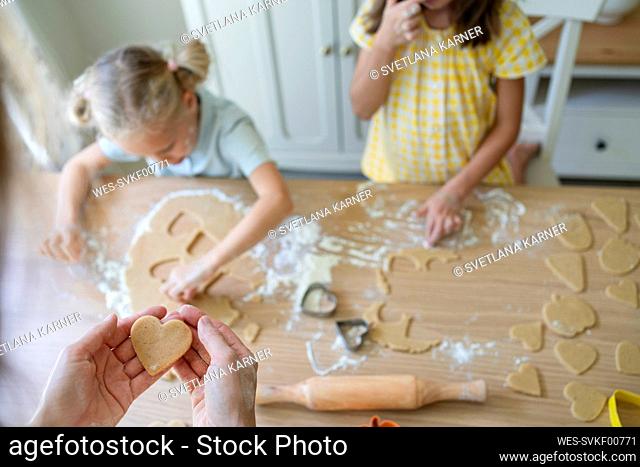 Hands of woman preparing cookies with girls at home