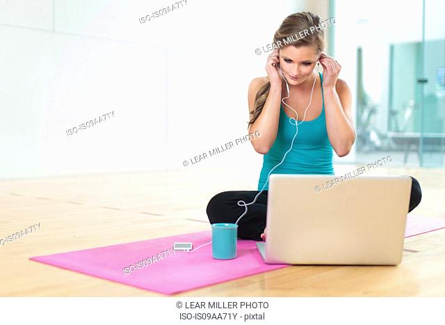Young woman on yoga mat listening to smartphone