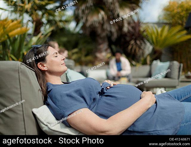 Serene pregnant woman relaxing on sunny patio lounge chair