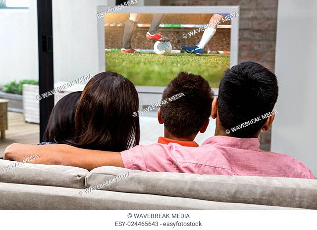 Composite image of happy family watching tv on the sofa