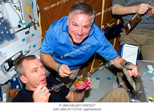 NASA astronauts Greg H. Johnson (top), STS-134 pilot; and Andrew Feustel, mission specialist, share a meal with their shuttle and station crewmates on the...