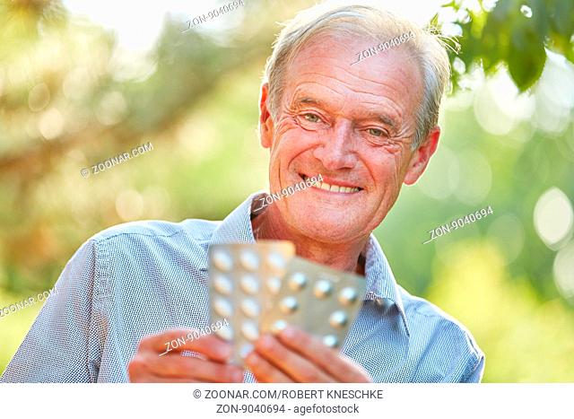 Alter Mann mit Medikamenten in der Hand lächelt zufrieden im Sommer