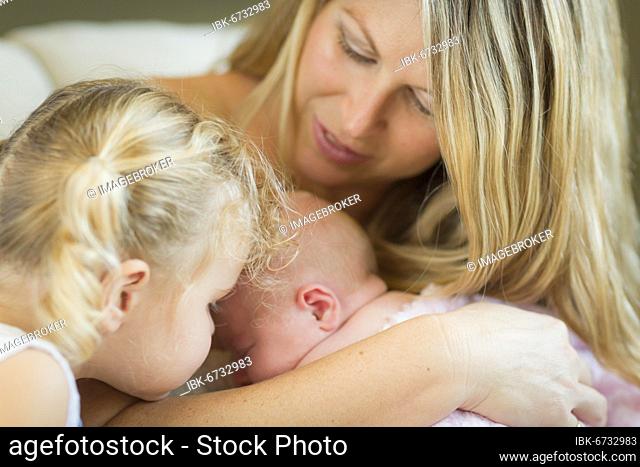 Beautiful young mother holds newborn baby girl as young sister looks on