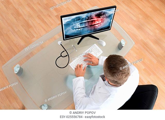 Young Doctor Examining Teeth X-ray On Computer At Desk