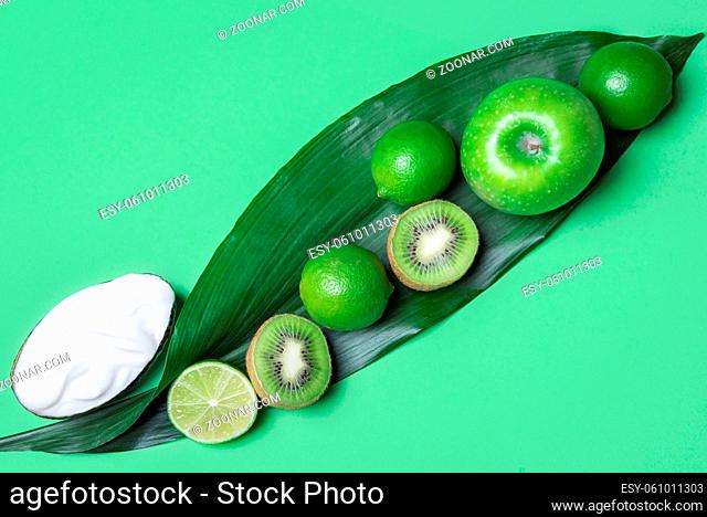 Above view of a green table with a mix of green fruits, apple, kiwi, limes on a big leaf and yogurt. Minimalist style. Healthy eating. Vegan food
