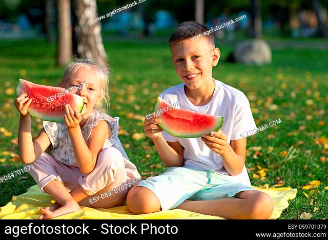 To cute kids lttle boy and girl eating juicy watermelon in the autumn park meadow