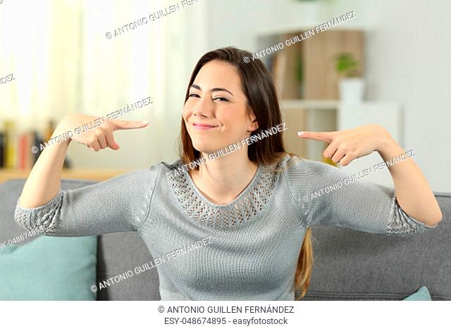 Front view portrait of a proud woman pointing herself sitting on a couch in the living room at home