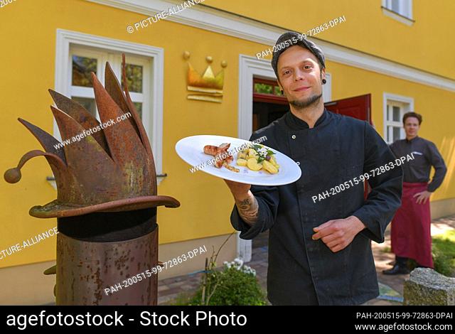 15 May 2020, Brandenburg, Kaisermühl: Sören Horny, chef at Hotel Kaisermühle, shows wild garlic sausages with potato caper salad on a plate