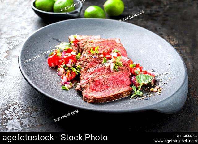 Traditional South American barbecue wagyu roast beef sliced with pico de gallo and salsa verde garnished as top view in a modern design plate