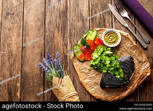 sandwich of black bread with vegetables on a wooden surface