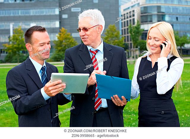 Drei lächelnde Geschäftsleute arbeiten im Park mit Tablet Computer und Smartphone