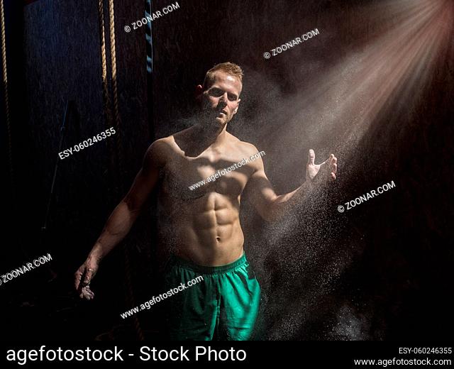 Shirtless man using chalk or magnesium powder in gym, clapping hands and creating cloud