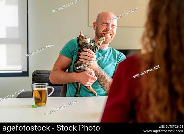 Happy man holding cat with woman at table
