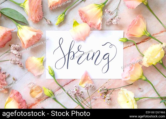 Card with the handwritten text SPRING surrounded by pink flowers, earrings, petals and parfume flacon top view on a marble table. Romantic concept