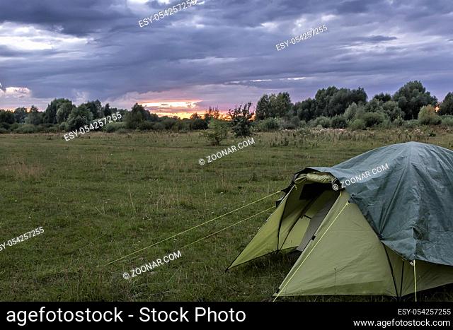 A small tourist tent in a clearing near the forest in the evening at sunset