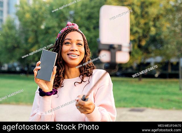 Smiling vlogger showing mobile phone while filming at park