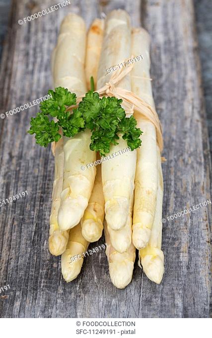 A bunch of white asparagus with parsley on a wooden surface
