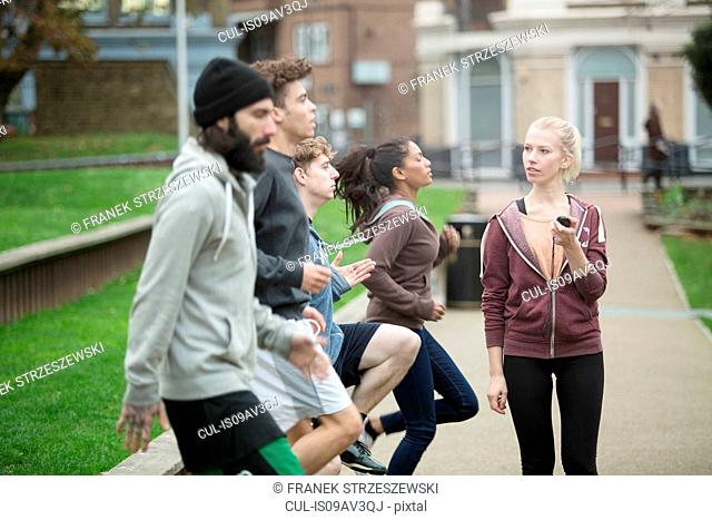 Group of adults exercising outdoors, young woman holding stopwatch