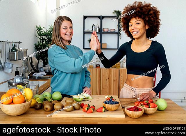 Happy women giving high-five to each other standing at table in kitchen