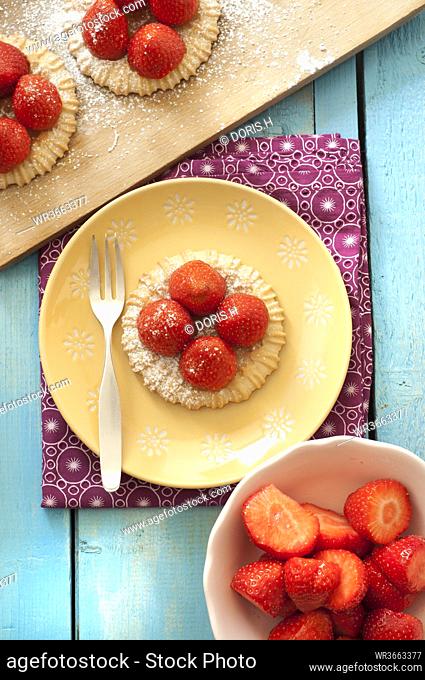 Strawberry tartlets on plate besides bowl of strawberry, close up