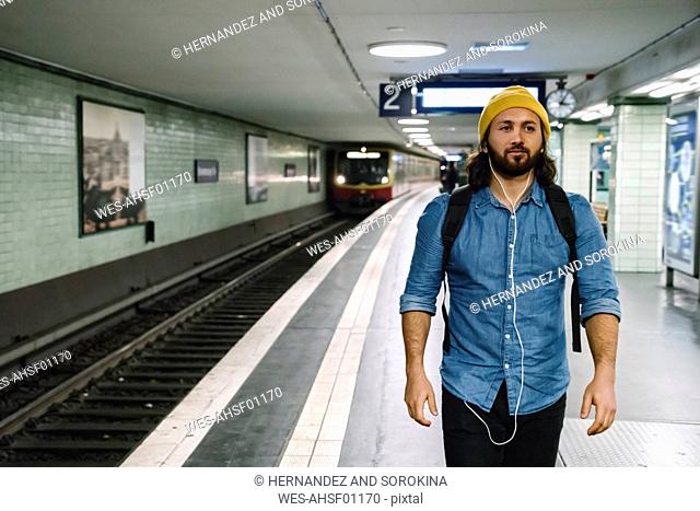 Portrait of man with backpack and earphones walking at platform, Berlin, Germany
