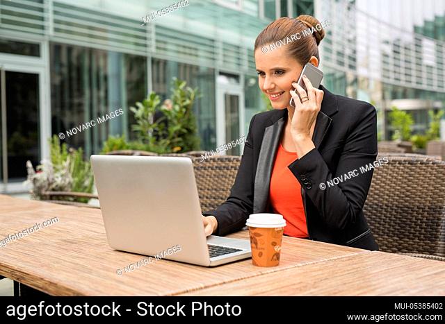 Young businesswoman using notebook and cell phones in cafe