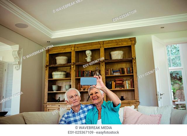 Senior couple taking a selfie on mobile phone in living room