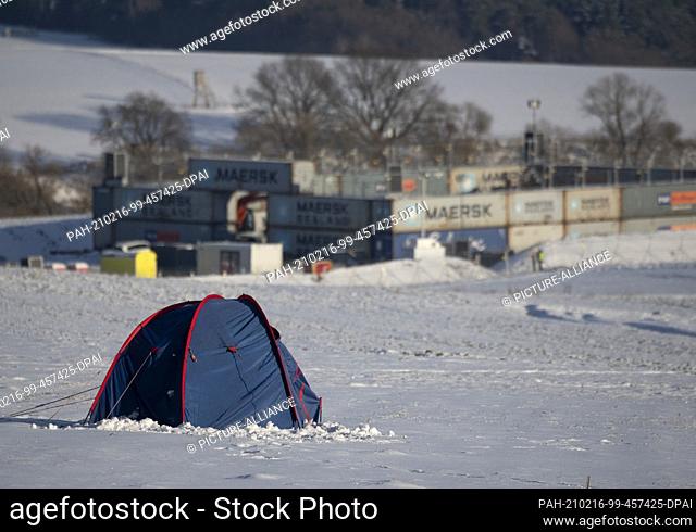 14 February 2021, Hessen, Dannenrod: Only one tent of motorway opponents stands on a snow-covered field in front of the machine depot of the construction...