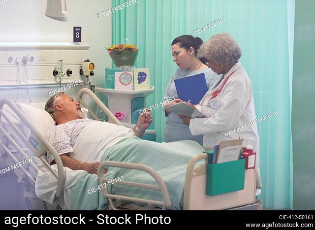 Doctors with medical chart making rounds, talking with senior patient in hospital room