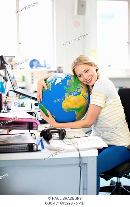 Smiling businessman hugging globe at desk in office