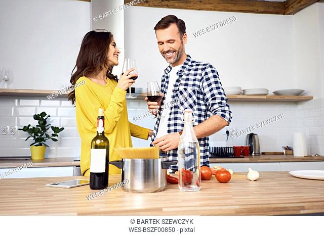 Affectionate couple in kitchen, preparing spaghetti toghether, drinking red wein