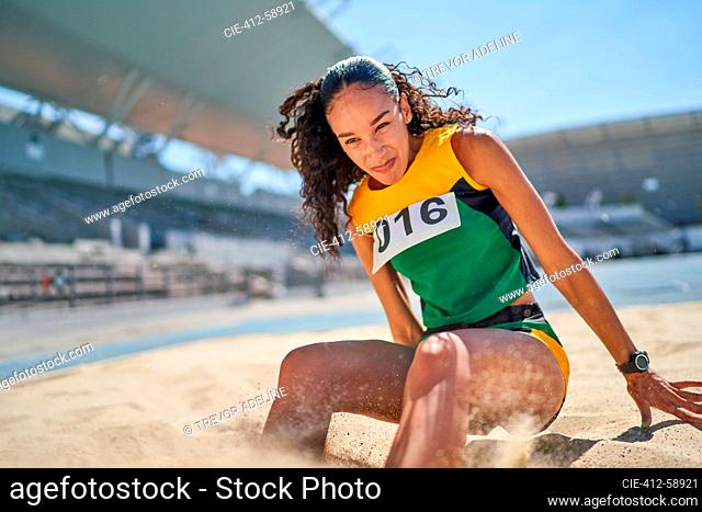 Female track and field athlete long jumping in sand