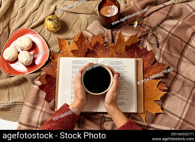 hands with cup of coffee, autumn leaves and book