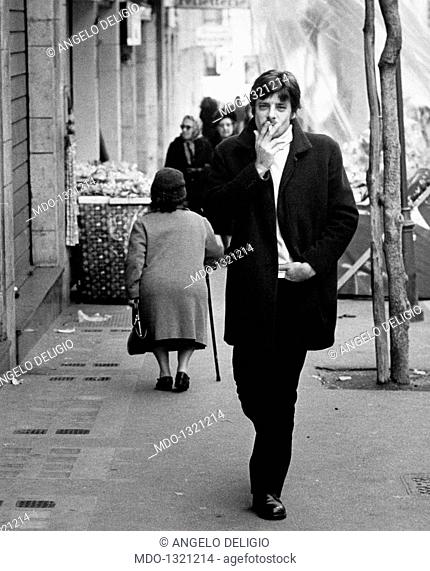 Giancarlo Giannini smoking a cigarette. The Italian actor and voice actor Giancarlo Giannini strolling in the city streets. He is smoking a cigarette