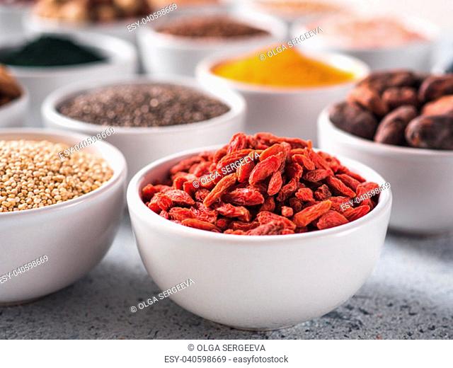 Goji berries in small white bowl and other superfoods on background. Selective focus. Different superfoods ingredients. Concept and illustration for superfood...