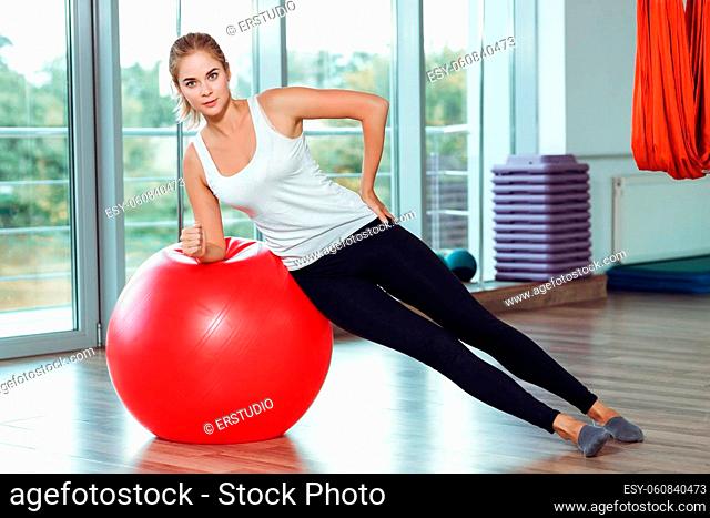 Young athletic woman doing exercises with red fitness ball in the gym