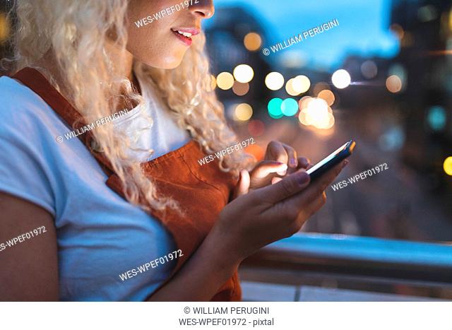Young woman in the city at dusk looking at her smartphone