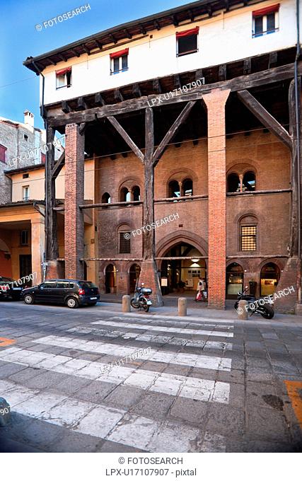 View across street pedestrian crossing showing medieval palazzo Casa Isolani, with Y-shaped oak beams holding up third floor and forming portico below