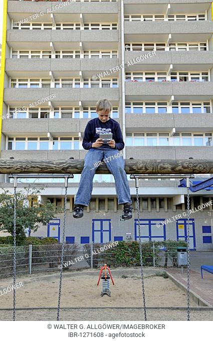 Boy, 9, playing with his Nintendo in front of a high-rise apartment building, satellite town of Chorweiler in Cologne, North Rhine-Westphalia, Germany, Europe