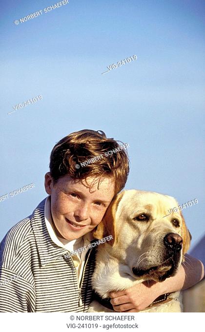 portrait, laughing freckeled boy with short red hair, 10 years, wearing t-shirt and trouser sits with his dog on a footbridge at the seaside  - GERMANY