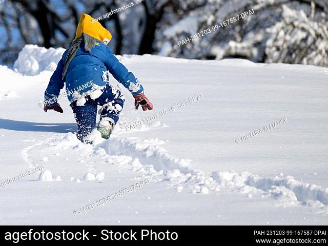 03 December 2023, Bavaria, Munich: A child runs through the snow in the Olympic Park. Snow and ice have caused chaos on the roads and on the railroads in...