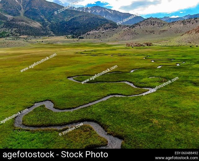Aerial view of green land and small curve river with mountain in the background in Aspen Springs, Mono County California, USA
