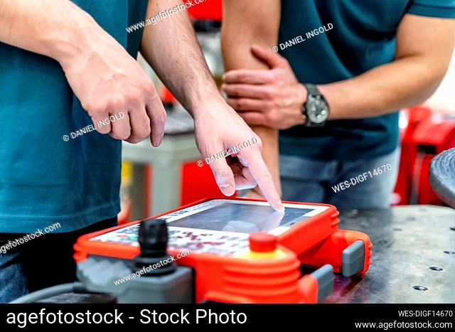 Young male engineer operating control by mature man at factory